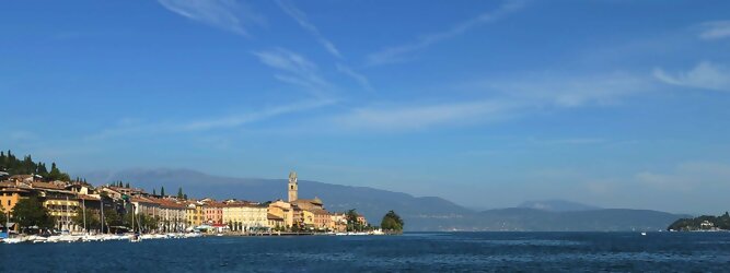 Rundreise beliebte Urlaubsziele am Gardasee -  Mit einer Fläche von 370 km² ist der Gardasee der größte See Italiens. Es liegt am Fuße der Alpen und erstreckt sich über drei Staaten: Lombardei, Venetien und Trentino. Die maximale Tiefe des Sees beträgt 346 m, er hat eine längliche Form und sein nördliches Ende ist sehr schmal. Dort ist der See von den Bergen der Gruppo di Baldo umgeben. Du trittst aus deinem gemütlichen Hotelzimmer und es begrüßt dich die warme italienische Sonne. Du blickst auf den atemberaubenden Gardasee, der in zahlreichen Blautönen schimmert - von tiefem Dunkelblau bis zu funkelndem Türkis. Majestätische Berge umgeben dich, während die Brise sanft deine Haut streichelt und der Duft von blühenden Zitronenbäumen deine Nase kitzelt. Du schlenderst die malerischen, engen Gassen entlang, vorbei an farbenfrohen, blumengeschmückten Häusern. Vereinzelt unterbricht das fröhliche Lachen der Einheimischen die friedvolle Stille. Du fühlst dich wie in einem Traum, der nicht enden will. Jeder Schritt führt dich zu neuen Entdeckungen und Abenteuern. Du probierst die köstliche italienische Küche mit ihren frischen Zutaten und verführerischen Aromen. Die Sonne geht langsam unter und taucht den Himmel in ein leuchtendes Orange-rot - ein spektakulärer Anblick.